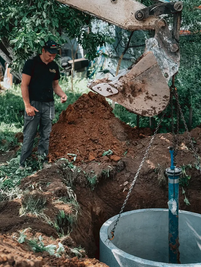 Excavator setting a concrete septic tank into an open trench during a system installation — illustrative stock photo, not an actual Pahrump job site